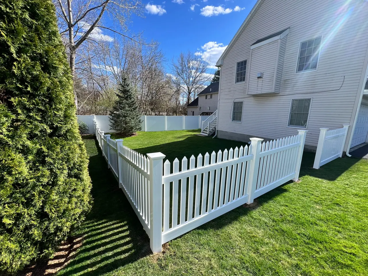 Decorative white vinyl picket fence surrounding a backyard lawn by DM Fence Inc