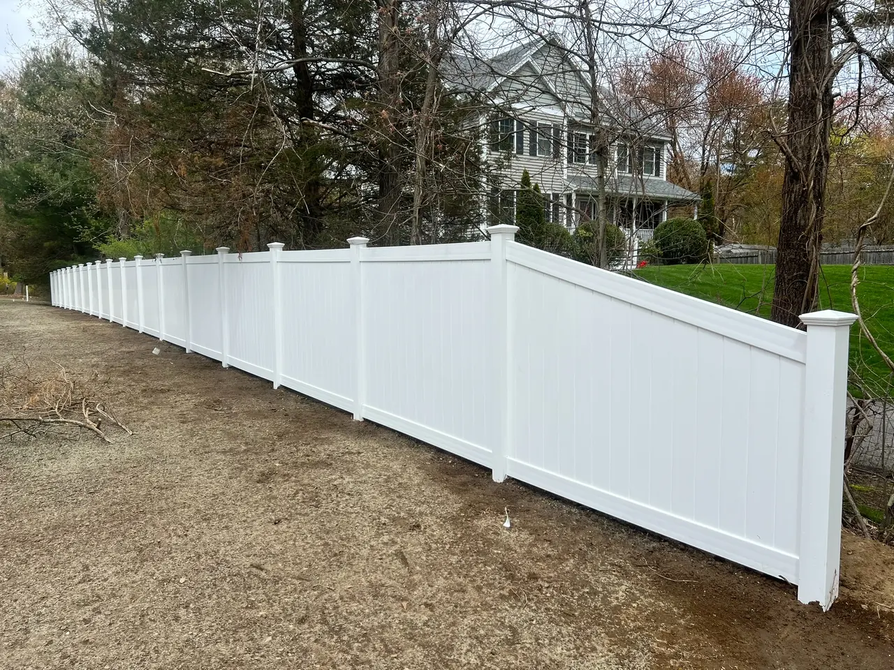 Close-up view of a white vinyl picket fence installed around a landscaped backyard by DM Fence Inc