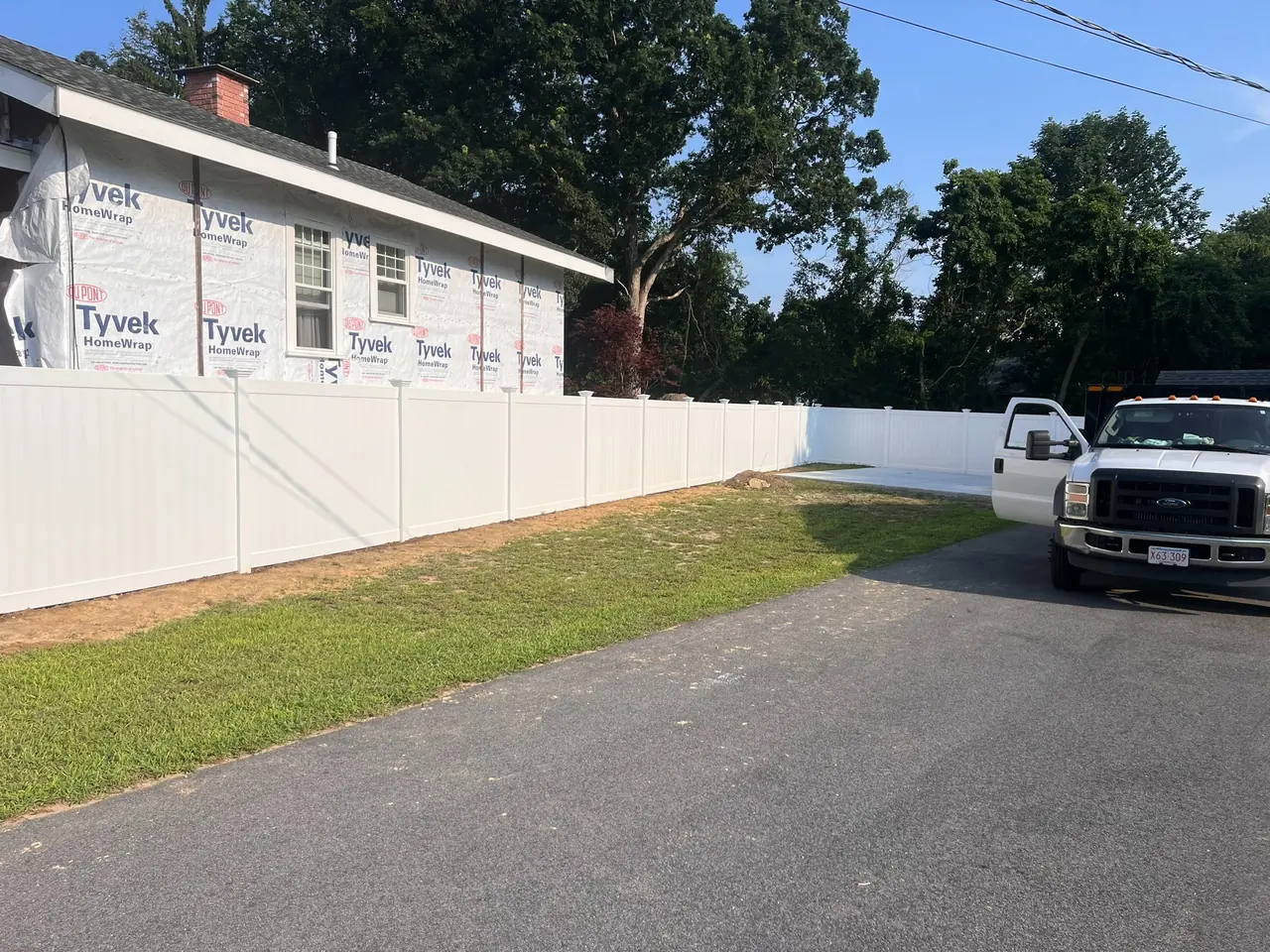 White vinyl privacy fence installation extending across a driveway and yard by DM Fence Inc