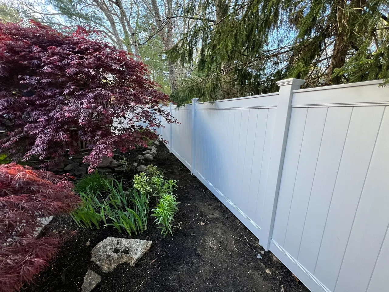 Long run of white vinyl privacy fence installed on a property line by DM Fence Inc